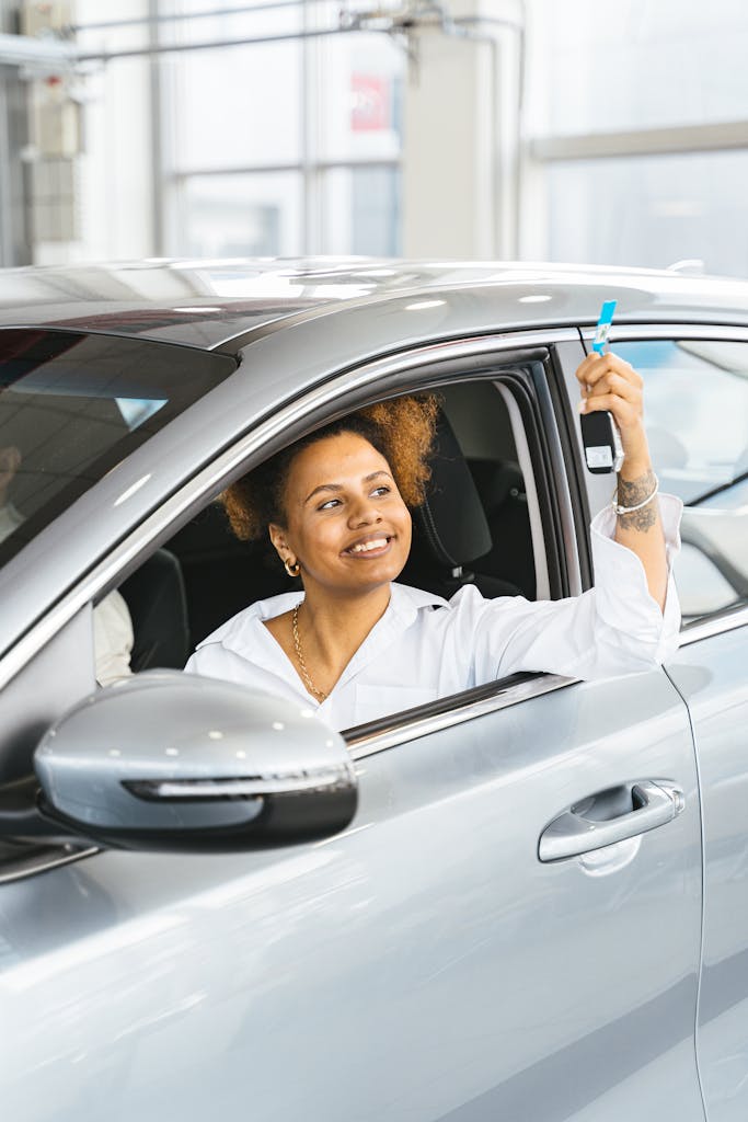 Smiling woman holding car keys from driver's seat in a new car